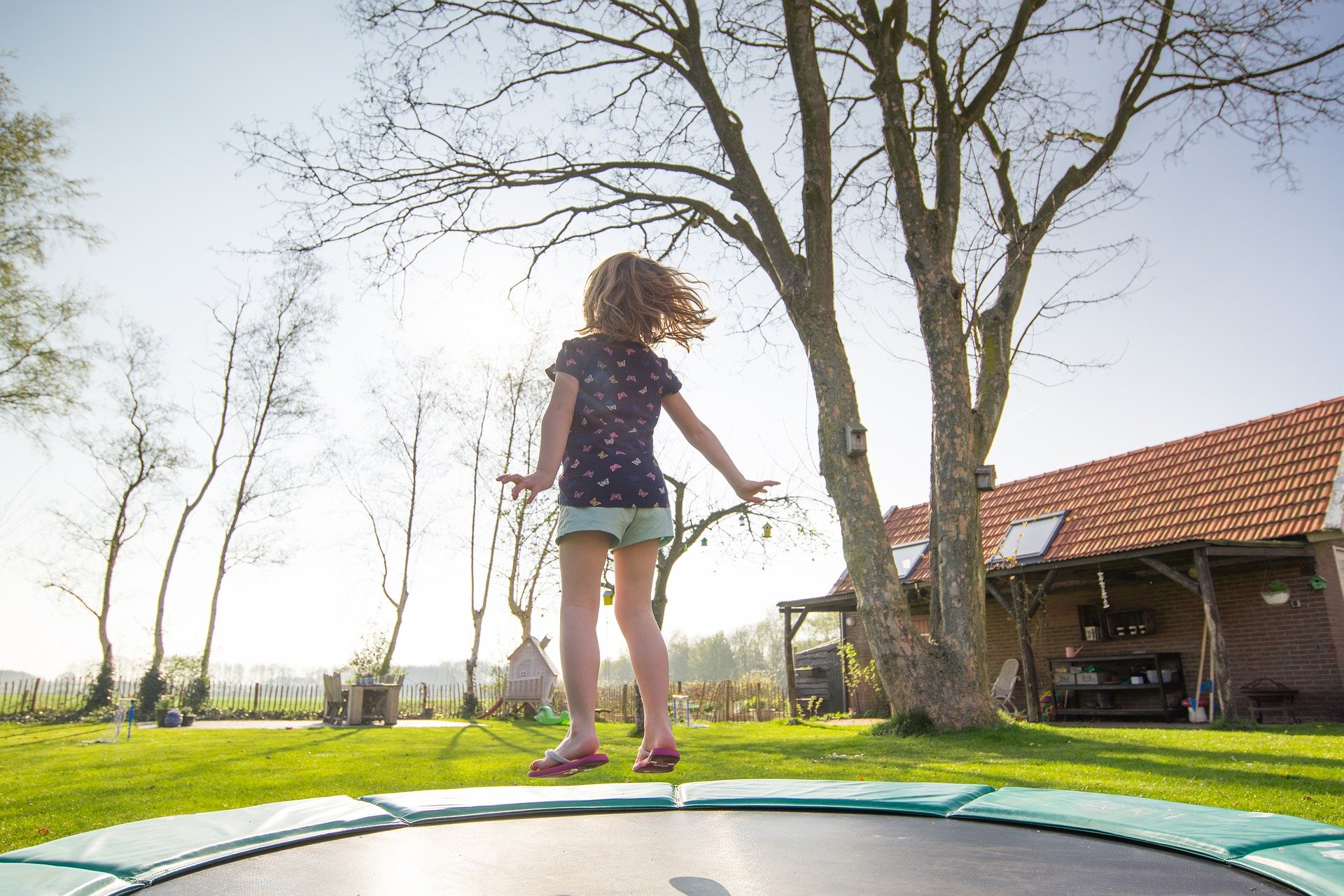 Dziecko skacze na trampolinie z Decathlonu w ogrodzie przy domu